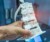 Close up mage of a persons hand holding a white 3D model of a portion of human spine inside a blurred printer room.